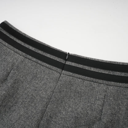 A woman wearing a grey herringbone matching set consisting of a top and shorts standing against a plain background