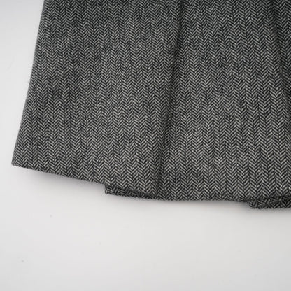 A woman wearing a grey herringbone pattern matching set consisting of a sleeveless top and shorts standing against a plain background