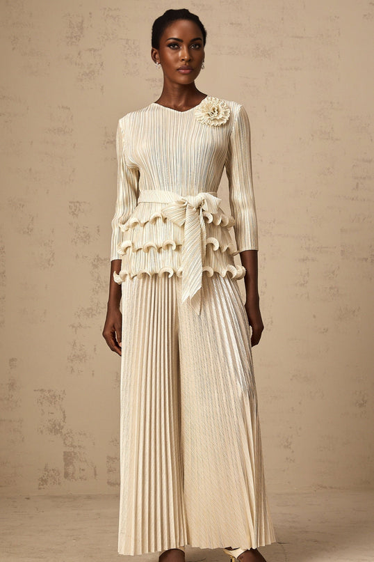 A woman wearing a jumpsuit with floral appliques and ruffled pleated details standing in a relaxed pose