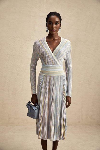 A woman wearing a kneelength knitted dress with vertical stripes standing in a relaxed pose the dress has a fitted silhouette and long sleeves showcasing the Amelie design
