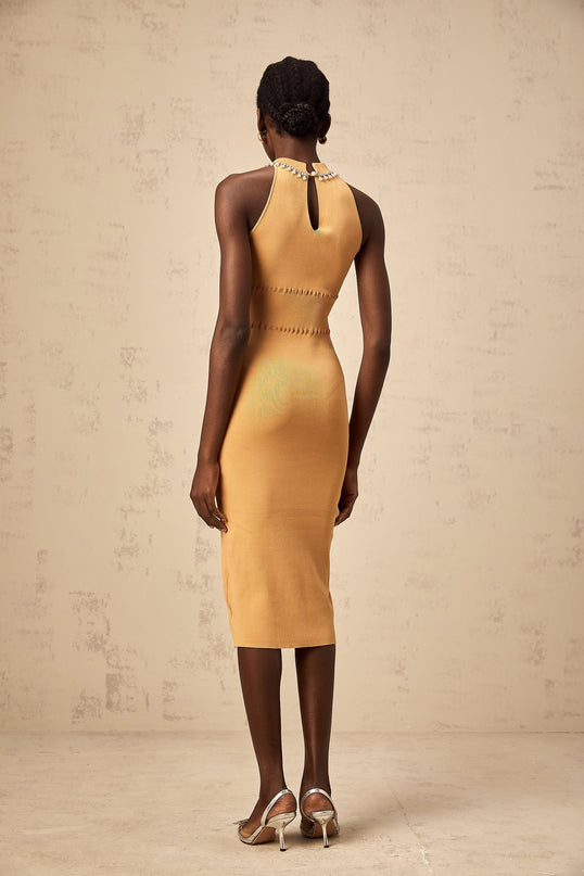 A woman wearing a knit midi dress in a light color with faux pearl embellishments scattered across the fabric the dress has a fitted silhouette and falls to mid calf length