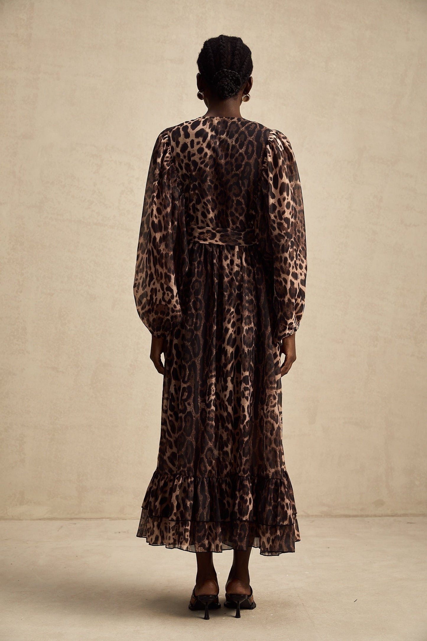 A woman wearing a leopard print midi dress with a single breasted design and a fitted silhouette standing in a neutral background
