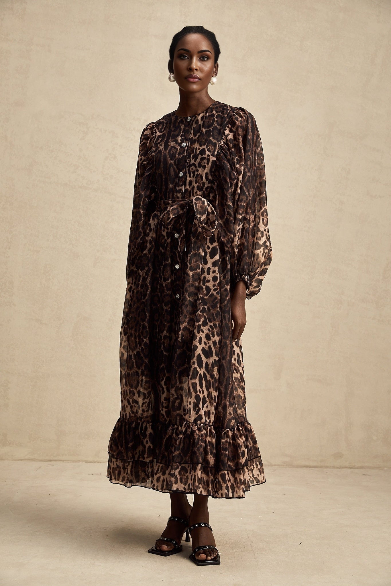 A woman wearing a leopard print midi dress with a single breasted design and long sleeves standing in a neutral pose