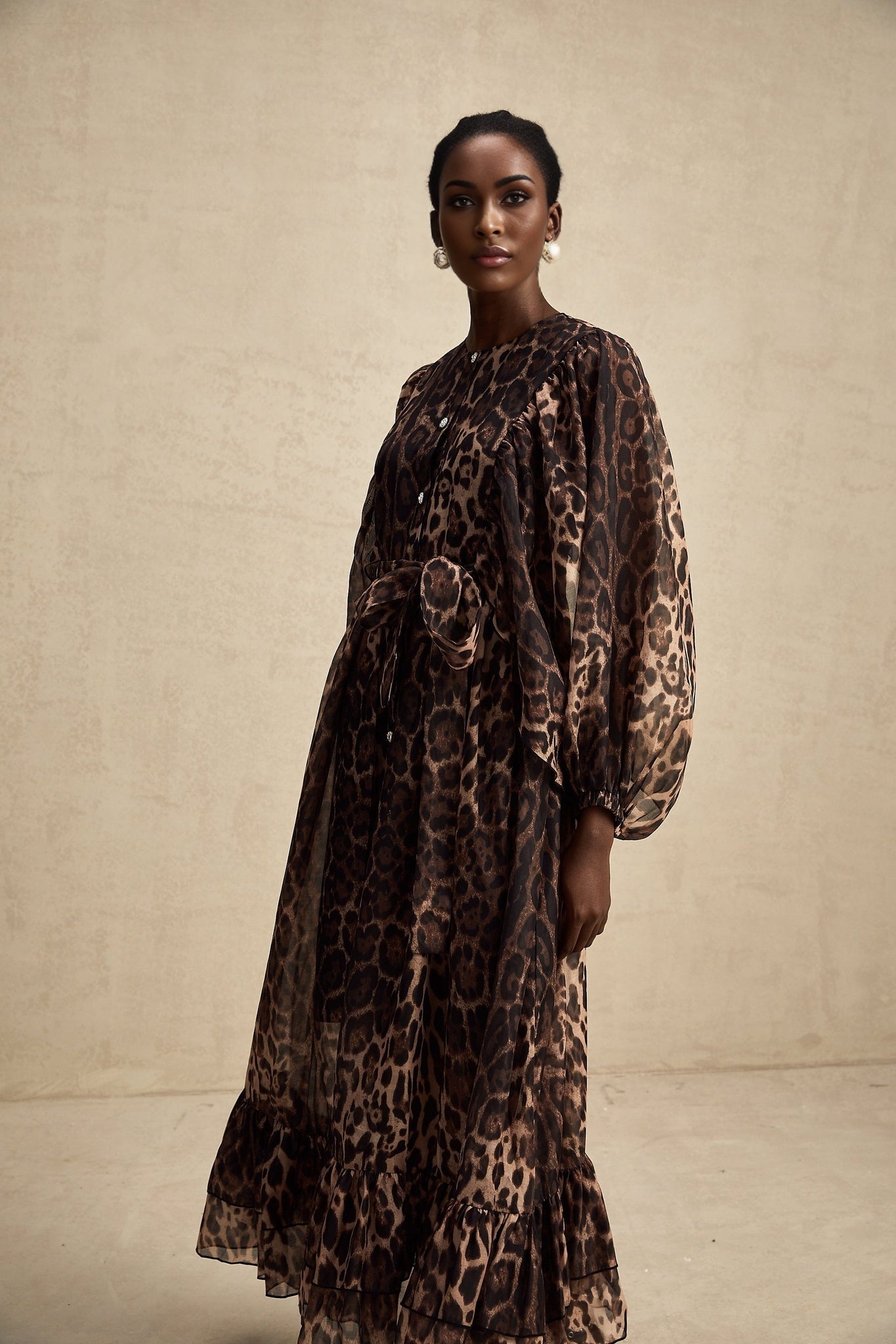 A woman wearing a leopard print midi dress with a single breasted design and long sleeves standing in a neutral pose