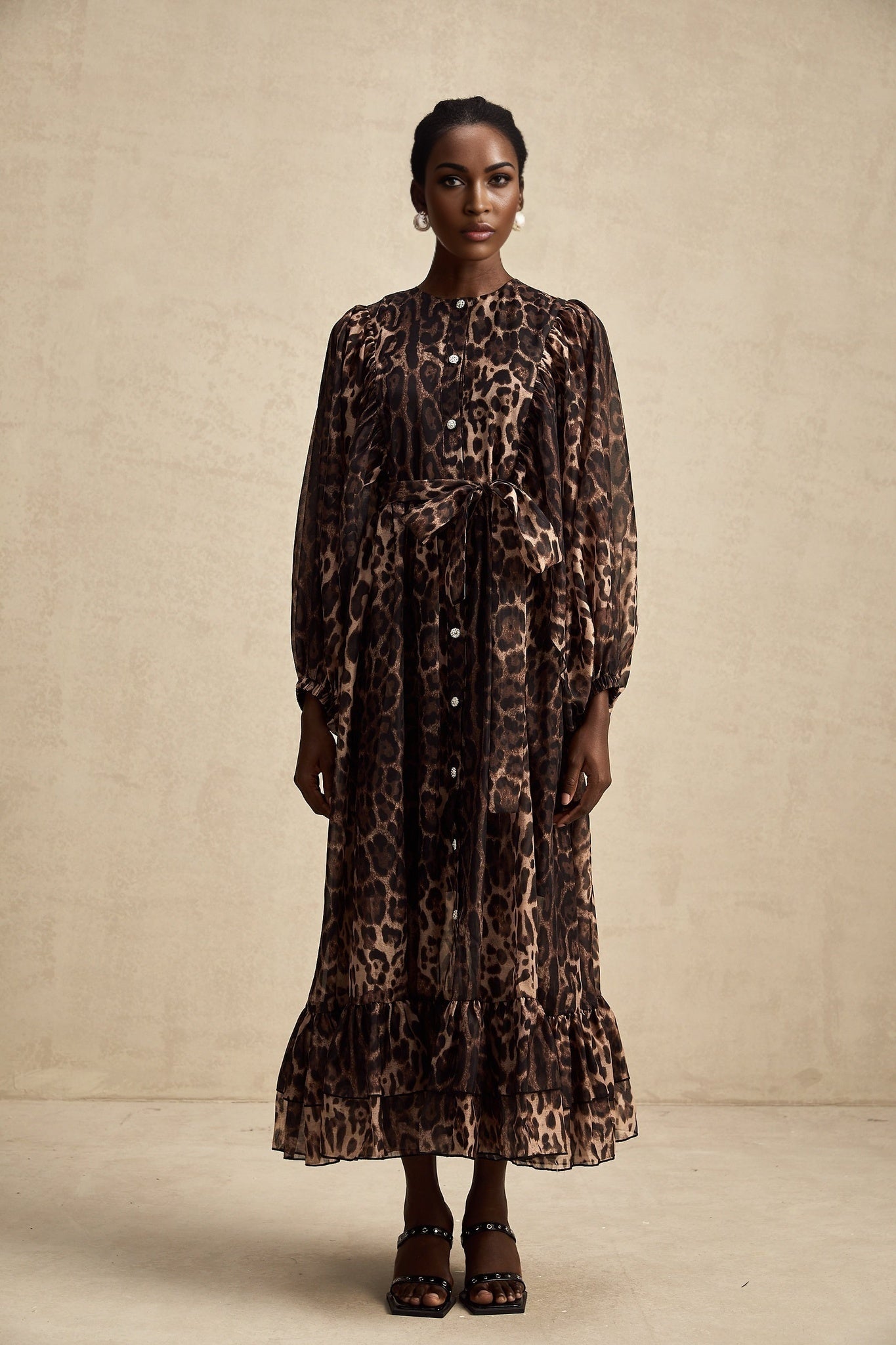 A woman wearing a leopard print midi dress with a single breasted design and long sleeves standing in a neutral pose