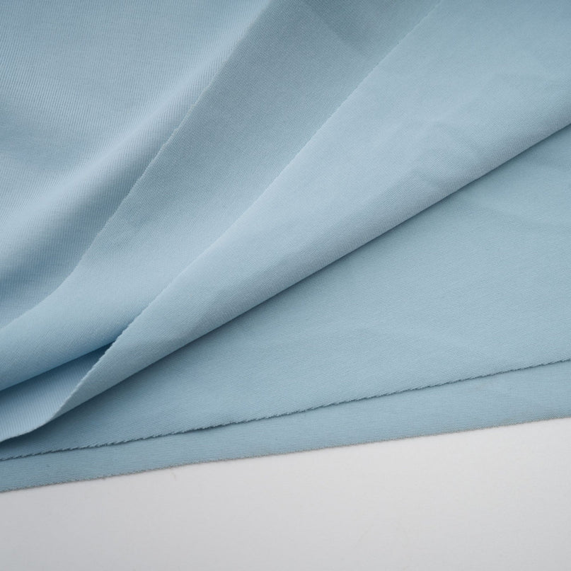 A woman wearing a light blue asymmetric maxi dress with pleated details The dress features a flowy skirt and an uneven hemline