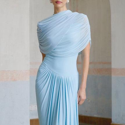A woman wearing a light blue asymmetric pleated maxi dress with a flowing skirt and one shoulder design