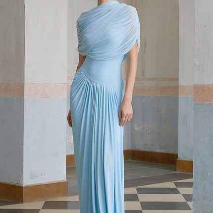 A woman wearing a light blue asymmetric pleated maxi dress with a flowy skirt and one shoulder design