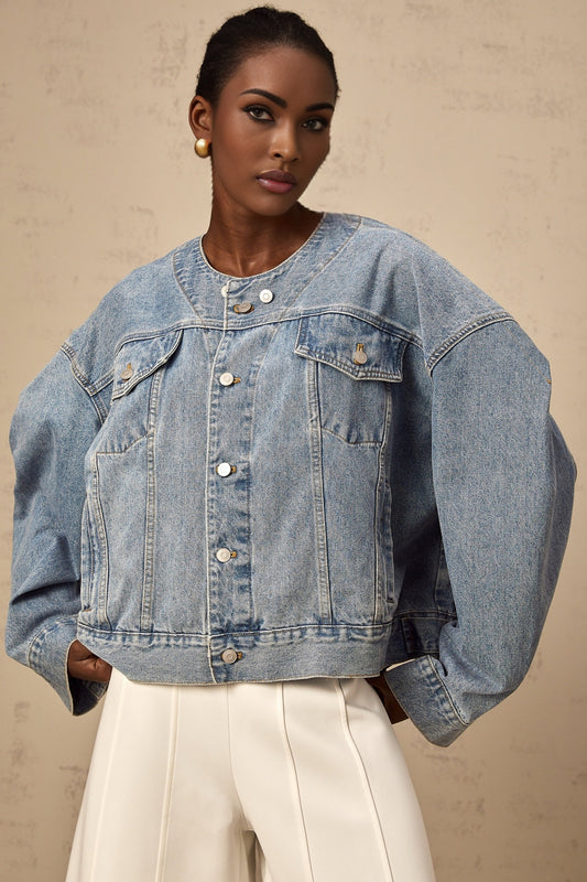 A woman wearing a light blue collarless denim jacket with front pockets and button closure