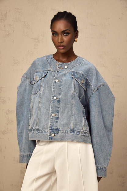 A woman wearing a light blue collarless denim jacket with long sleeves and front pockets