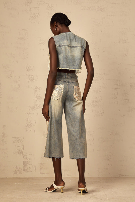 A woman wearing a light blue cropped denim top with lace panelling details visible on the shoulders and sides