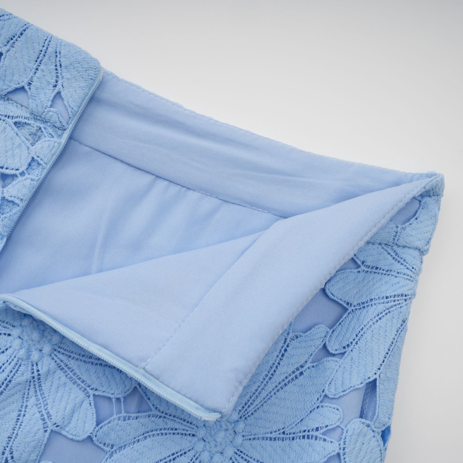 A woman wearing a light blue matching set consisting of a lace top and skirt with intricate floral guipure patterns standing against a plain background