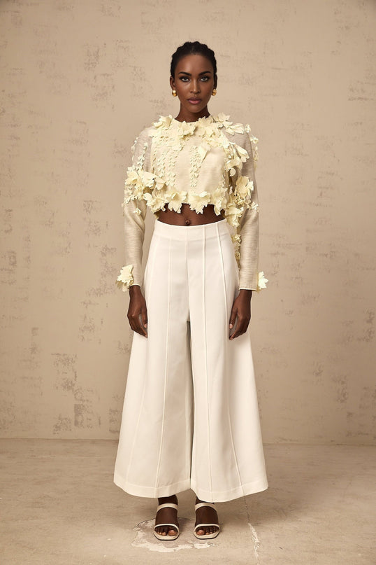 A woman wearing a light yellow cropped blouse with three dimensional floral petal details on the front