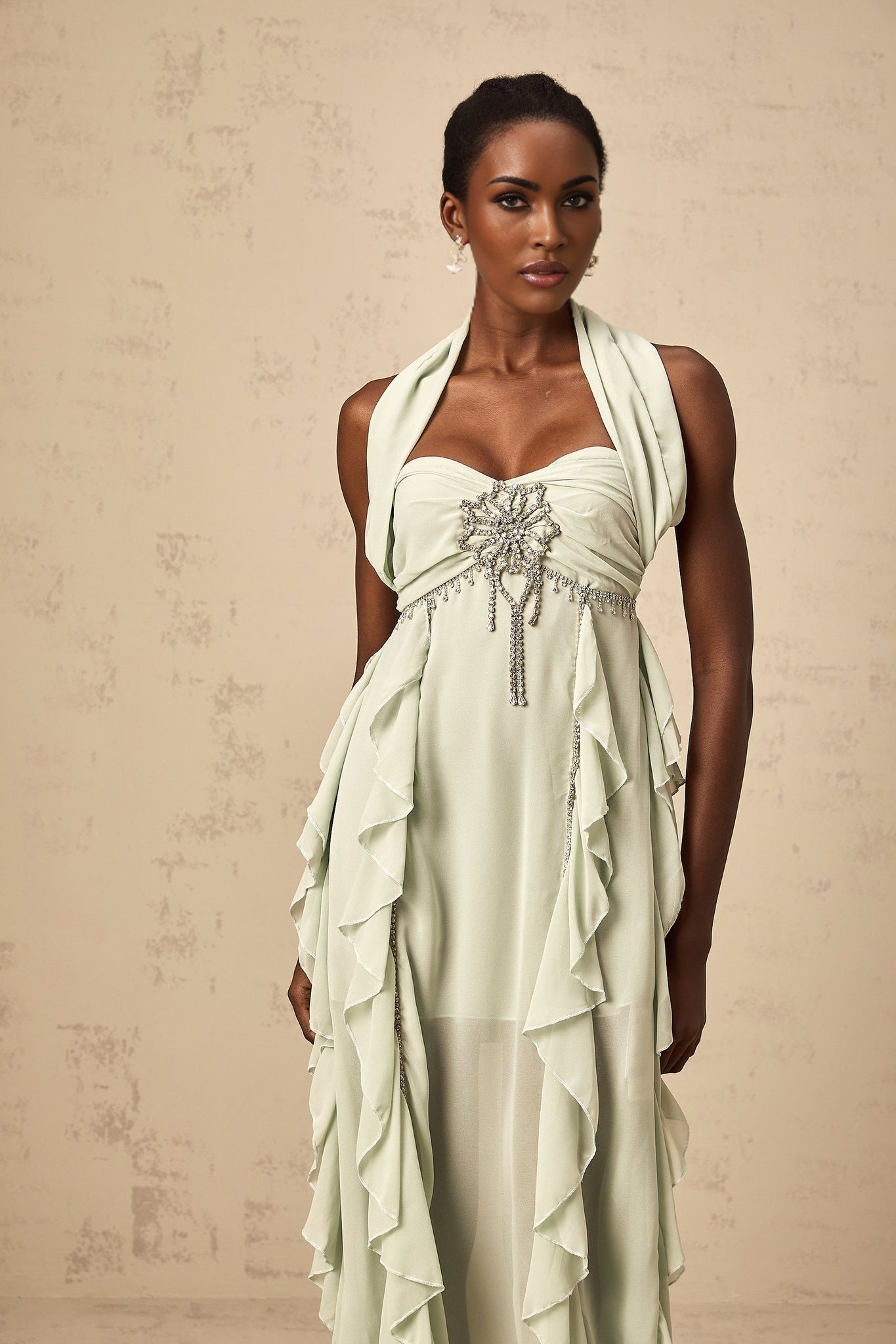 A woman wearing a lightcolored midi dress with ruffled details and embellishments standing in a neutral background