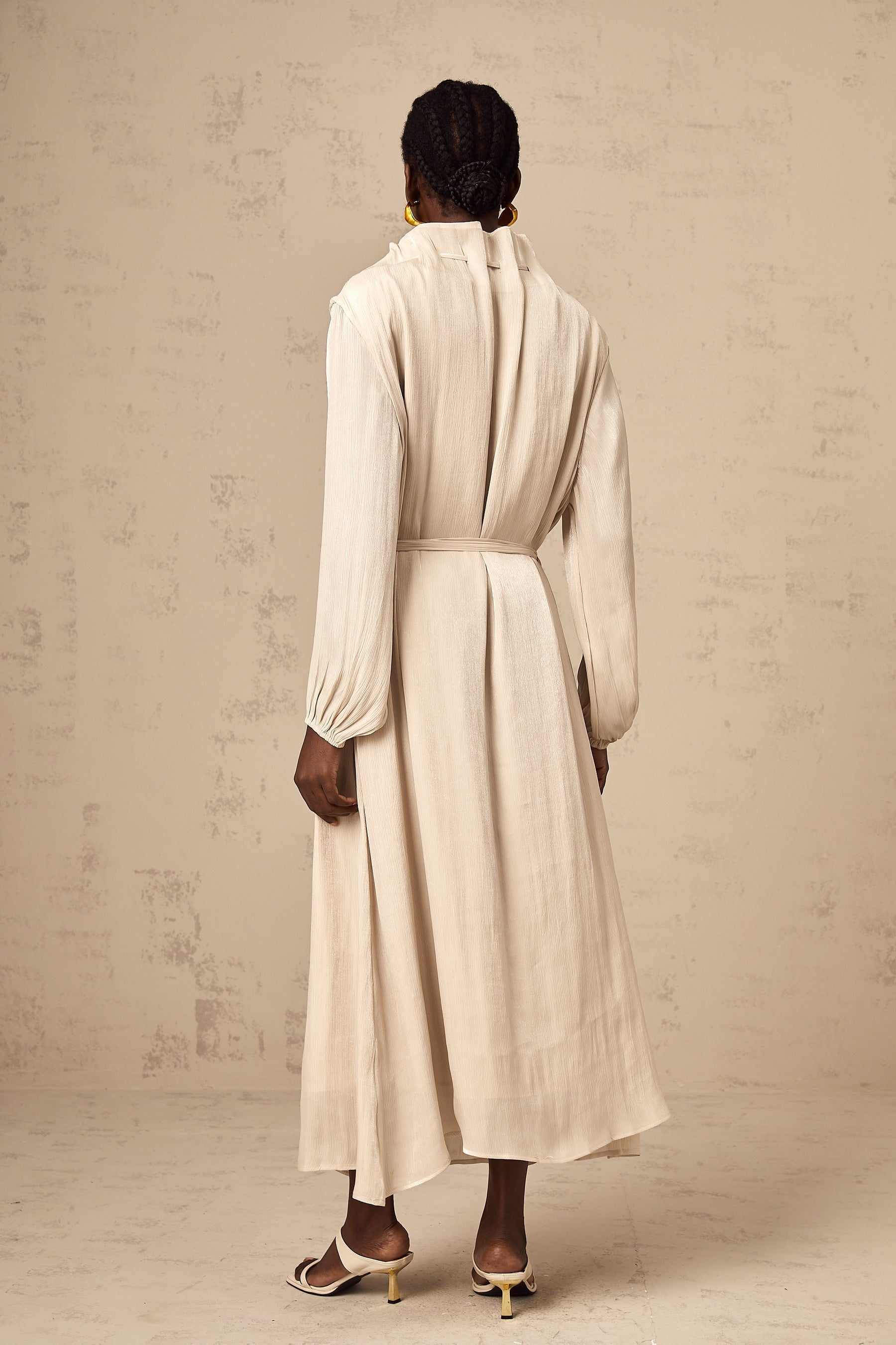 A woman wearing a lightcolored tulle midi dress with a selftie waist standing in a neutral background