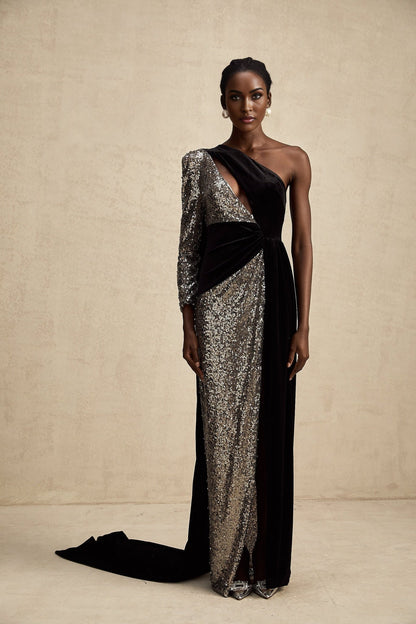 A woman wearing a long asymmetrical maxi dress with allover sequin embellishment shimmering in the light The dress features a high slit on one side revealing the leg