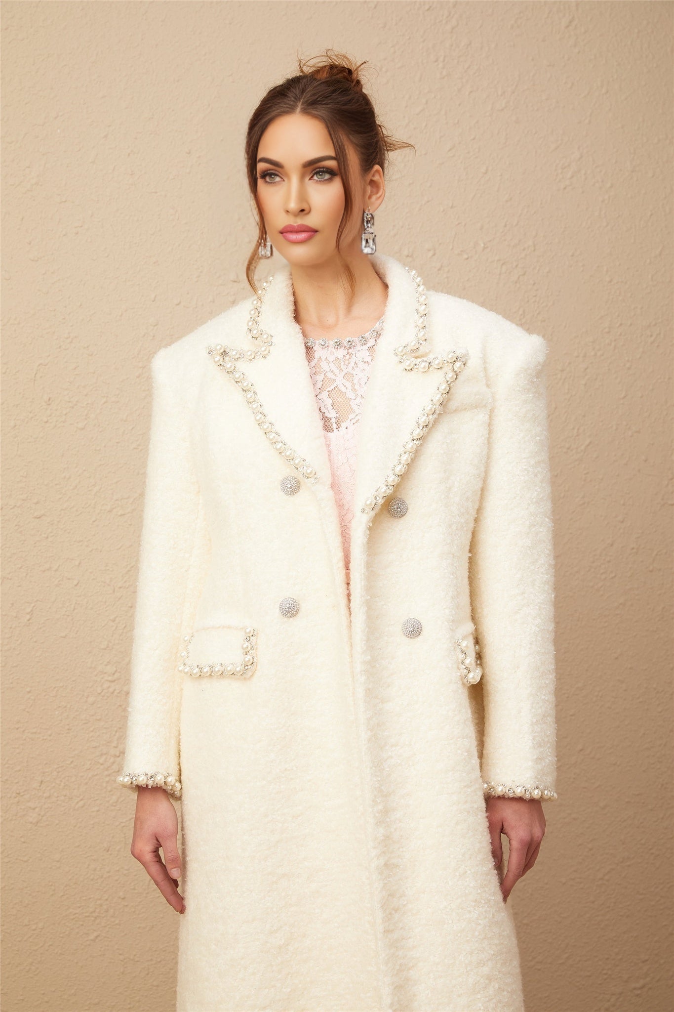 A woman wearing a long beige tweed coat with faux pearl embellishments on the collar and cuffs