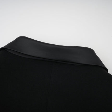 A woman wearing a long black blazer dress with embellishments and a maxi length silhouette