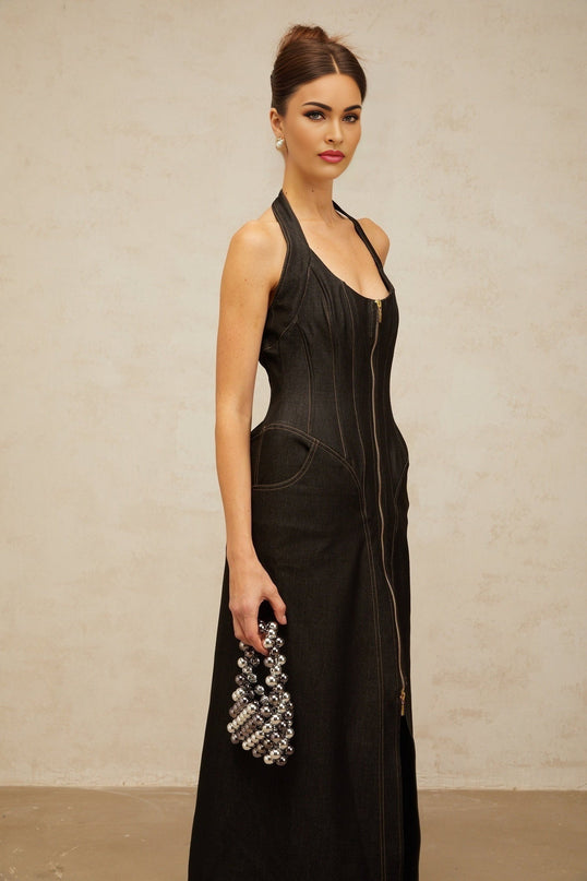 A woman wearing a long black denim maxi dress with a front slit and visible contrast stitching standing in a casual pose