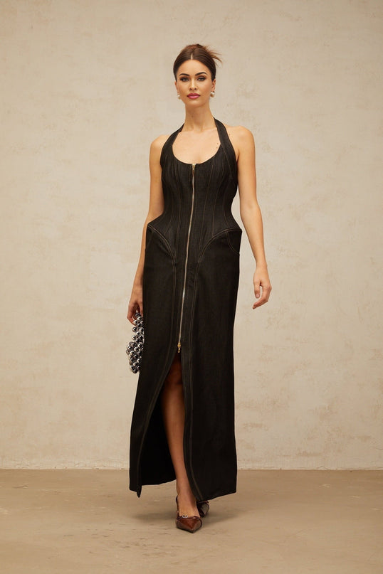 A woman wearing a long black denim maxi dress with contrast stitching and a front slit standing against a plain background