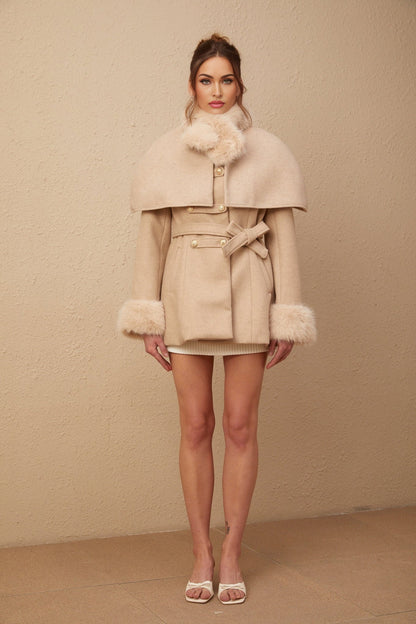 A woman wearing a long black faux fur coat with a detachable cape around the shoulders standing in a stylish pose