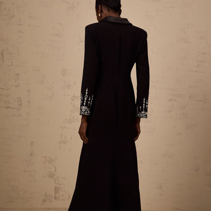 A woman wearing a long black maxi blazer dress with embellished details standing in a neutral pose