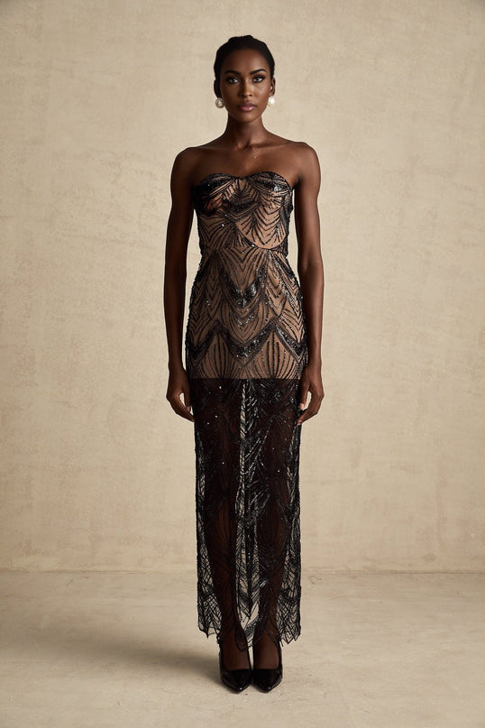 A woman wearing a long black maxi dress with a sequinned corset bodice and sheer mesh skirt