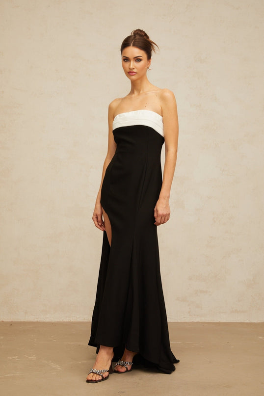 A woman wearing a long black maxi dress with colorblock details and an offshoulder neckline