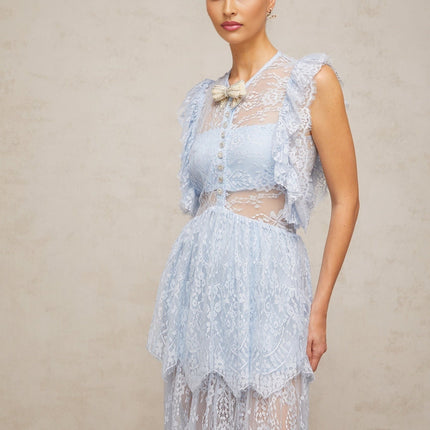 A woman wearing a long blue lace maxi dress with layered skirt and delicate floral pattern standing against a plain background