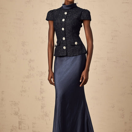 A woman wearing a long blue maxi dress with a fitted peplum waist and panelled design featuring a flowy skirt and sleeveless bodice