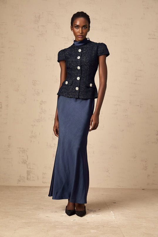 A woman wearing a long blue maxi dress with a fitted peplum waist and panelled design The dress features a flowy skirt and elegant silhouette