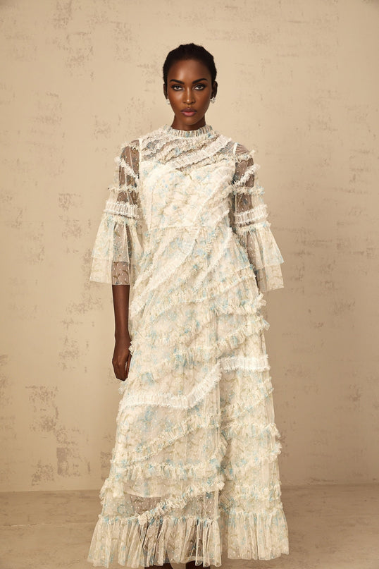 A woman wearing a long blue maxi dress with a floral print and ruffled tulle details