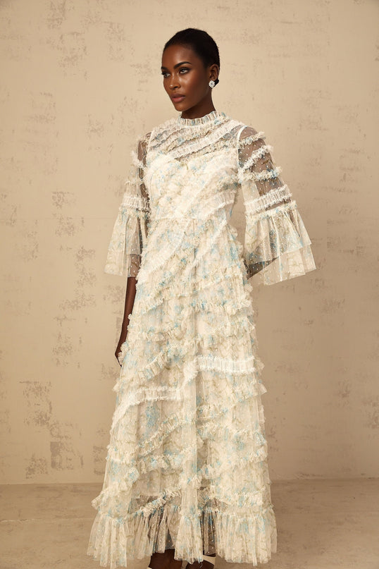 A woman wearing a long blue maxi dress with a floral print and ruffled tulle details