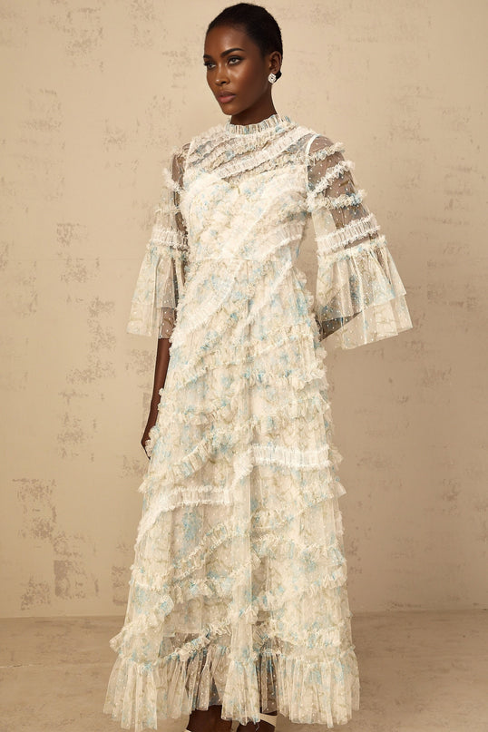 A woman wearing a long blue maxi dress with a floral print pattern and ruffled tulle details