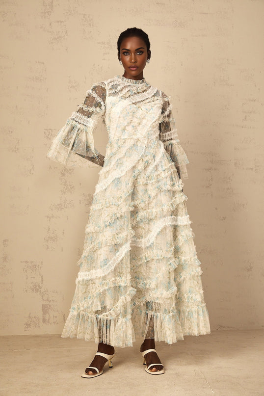 A woman wearing a long blue maxi dress with a floral print pattern and ruffled tulle details