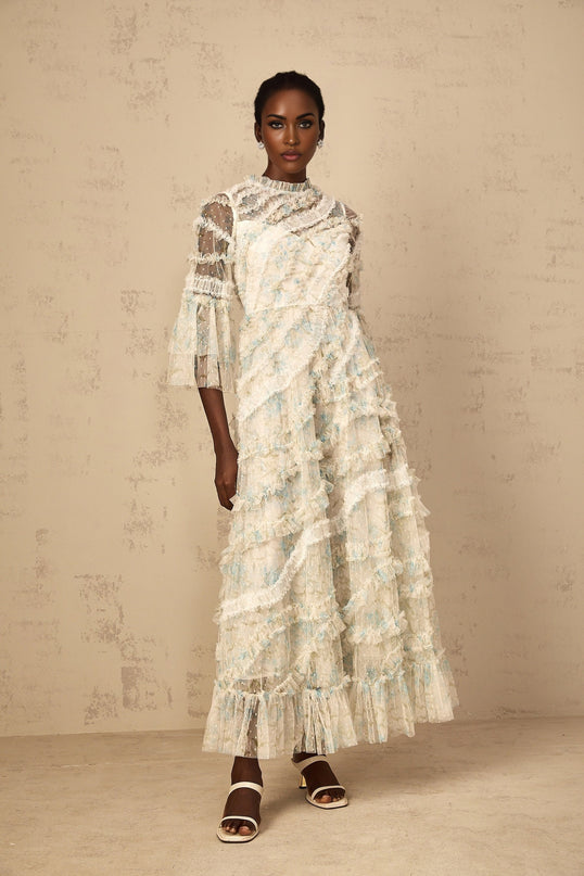 A woman wearing a long blue maxi dress with a floral print pattern and ruffled tulle details