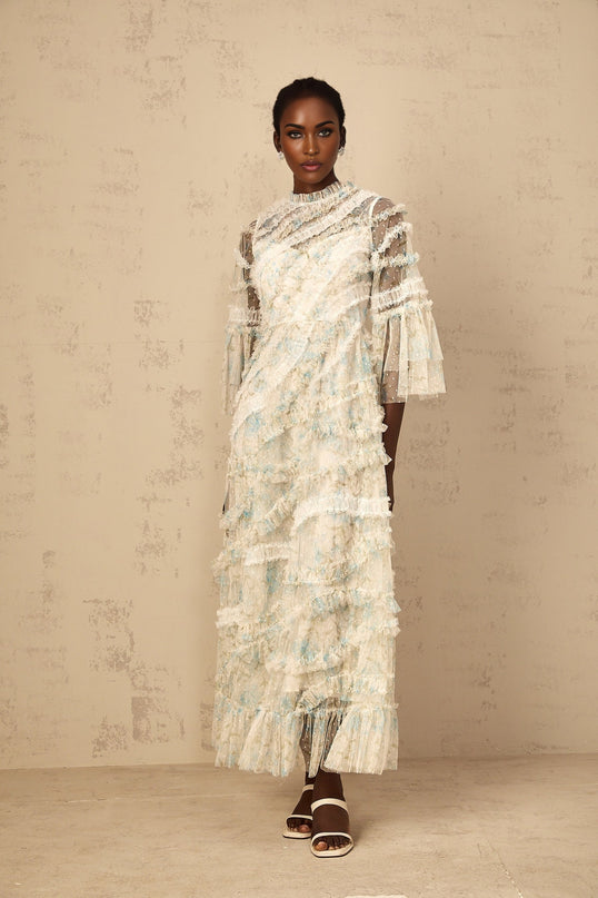 A woman wearing a long blue maxi dress with floral print and ruffled tulle details