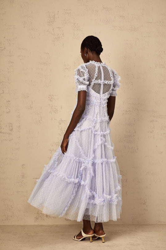 A woman wearing a long blue maxi dress with white polka dots and ruffled tulle details