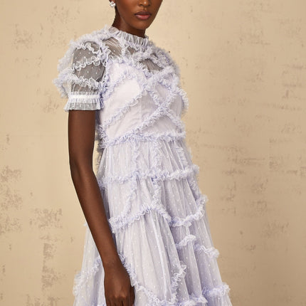 A woman wearing a long blue maxi dress with white polka dots and ruffled tulle details