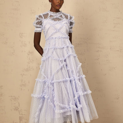 A woman wearing a long blue maxi dress with white polka dots and ruffled tulle details