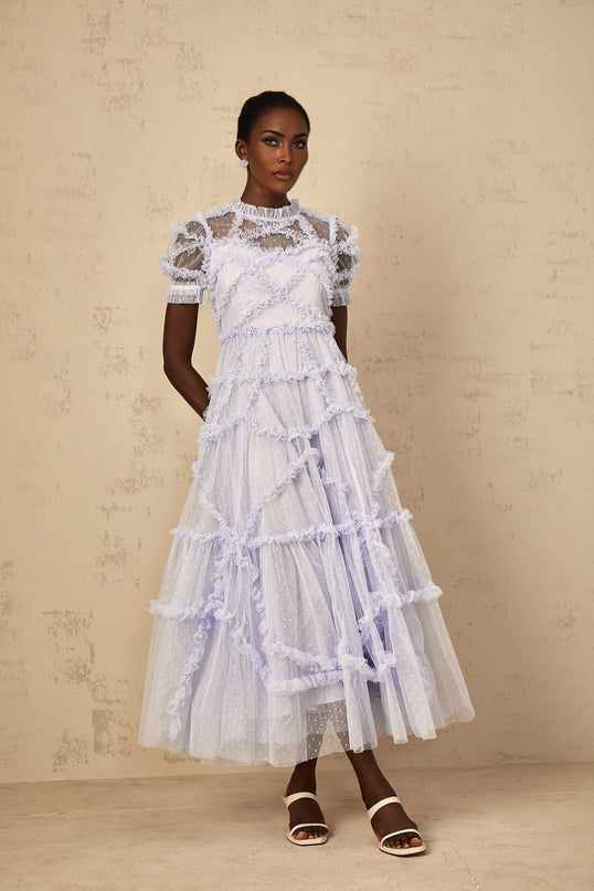 A woman wearing a long blue maxi dress with white polka dots and ruffled tulle details