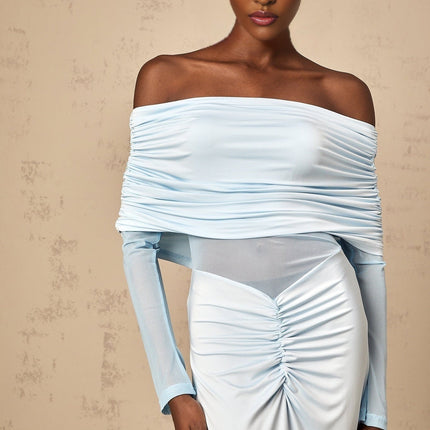 A woman wearing a long blue offshoulder dress with ruched detailing standing against a plain background