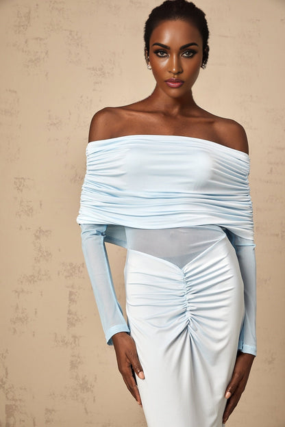A woman wearing a long blue offshoulder dress with ruched detailing standing against a plain background