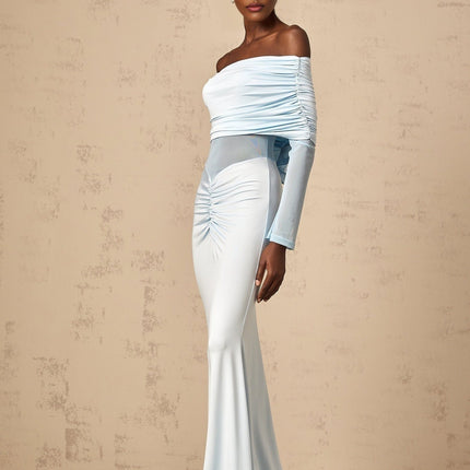 A woman wearing a long blue offshoulder dress with ruched detailing standing against a plain background