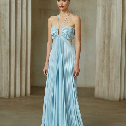 A woman wearing a long blue pleated maxi dress with a cutout detail standing against a plain background