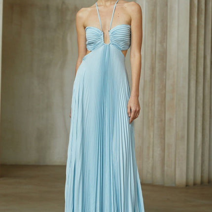 A woman wearing a long blue pleated maxi dress with a cutout detail standing in a relaxed pose against a plain background