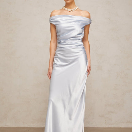 A woman wearing a long blue satin dress with offshoulder sleeves and ruched detailing standing in an elegant pose