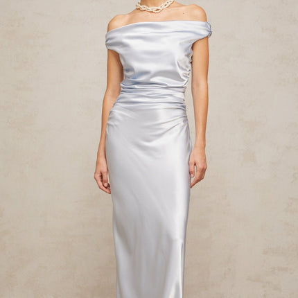 A woman wearing a long blue satin dress with offshoulder sleeves and ruched detailing standing in an elegant pose