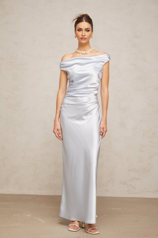 A woman wearing a long blue satin maxi dress with off the shoulder sleeves and ruched detailing