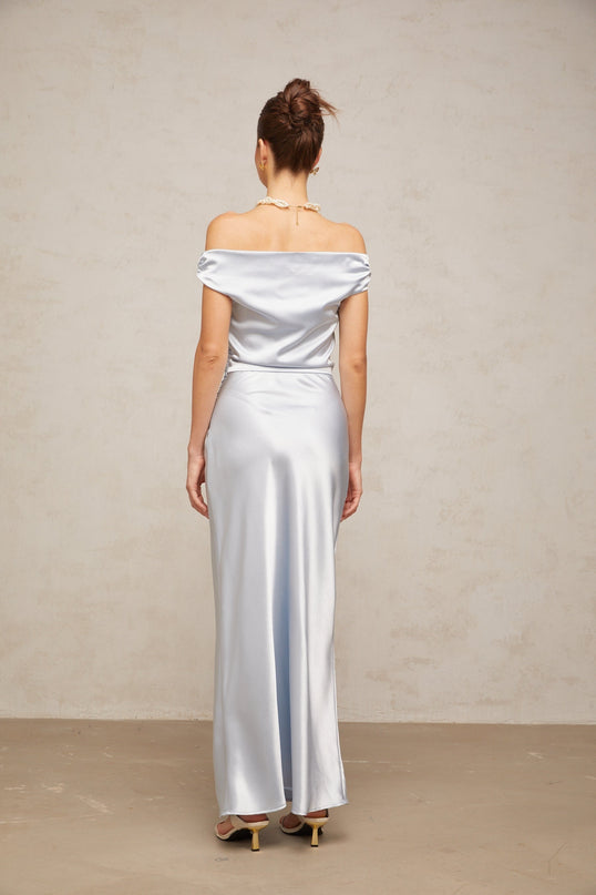 A woman wearing a long blue satin maxi dress with offshoulder sleeves and ruched detailing